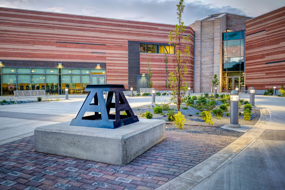 Four metal, block A's on a concrete stand lean towards each other at the top and connect in front of the classroom and student services building.