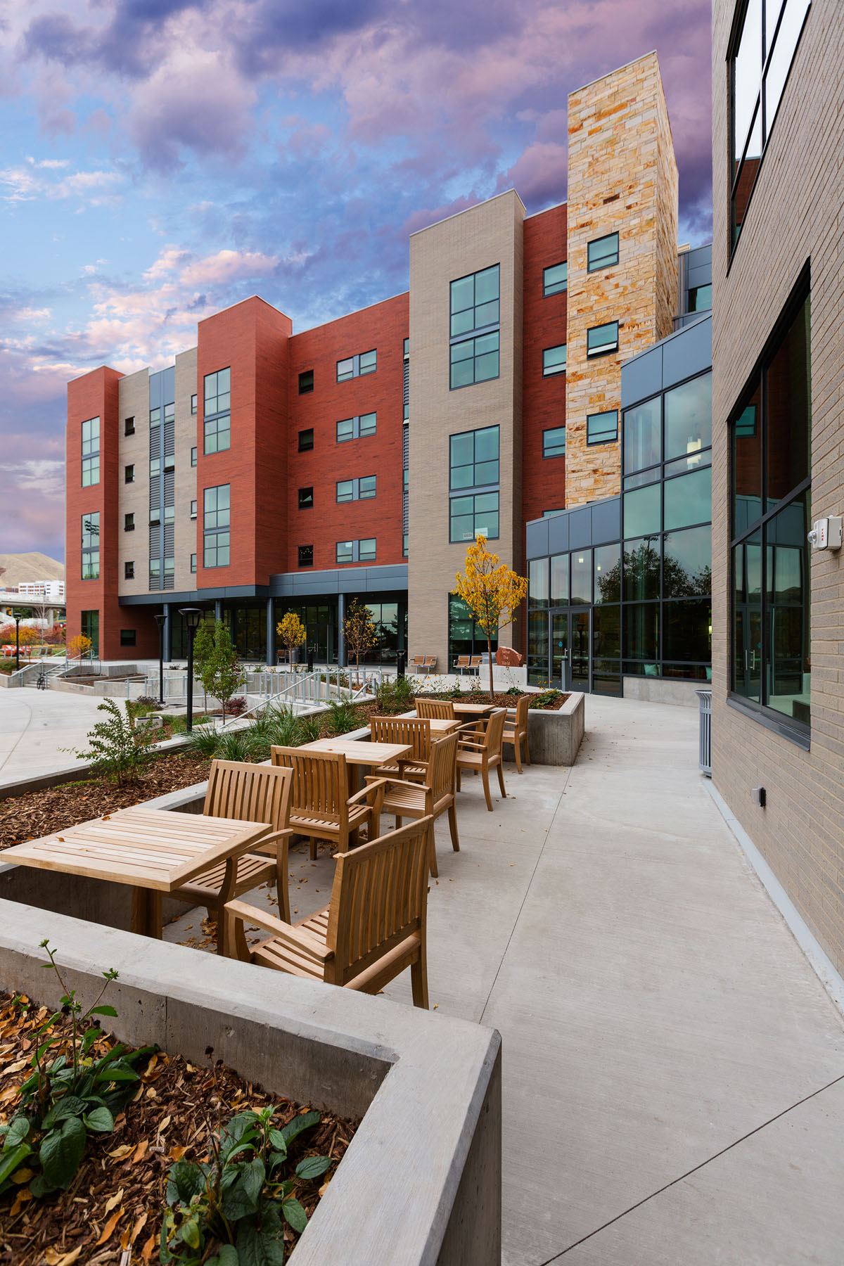 Outdoor wood tables and chairs near the main entrance to the honors student housing.